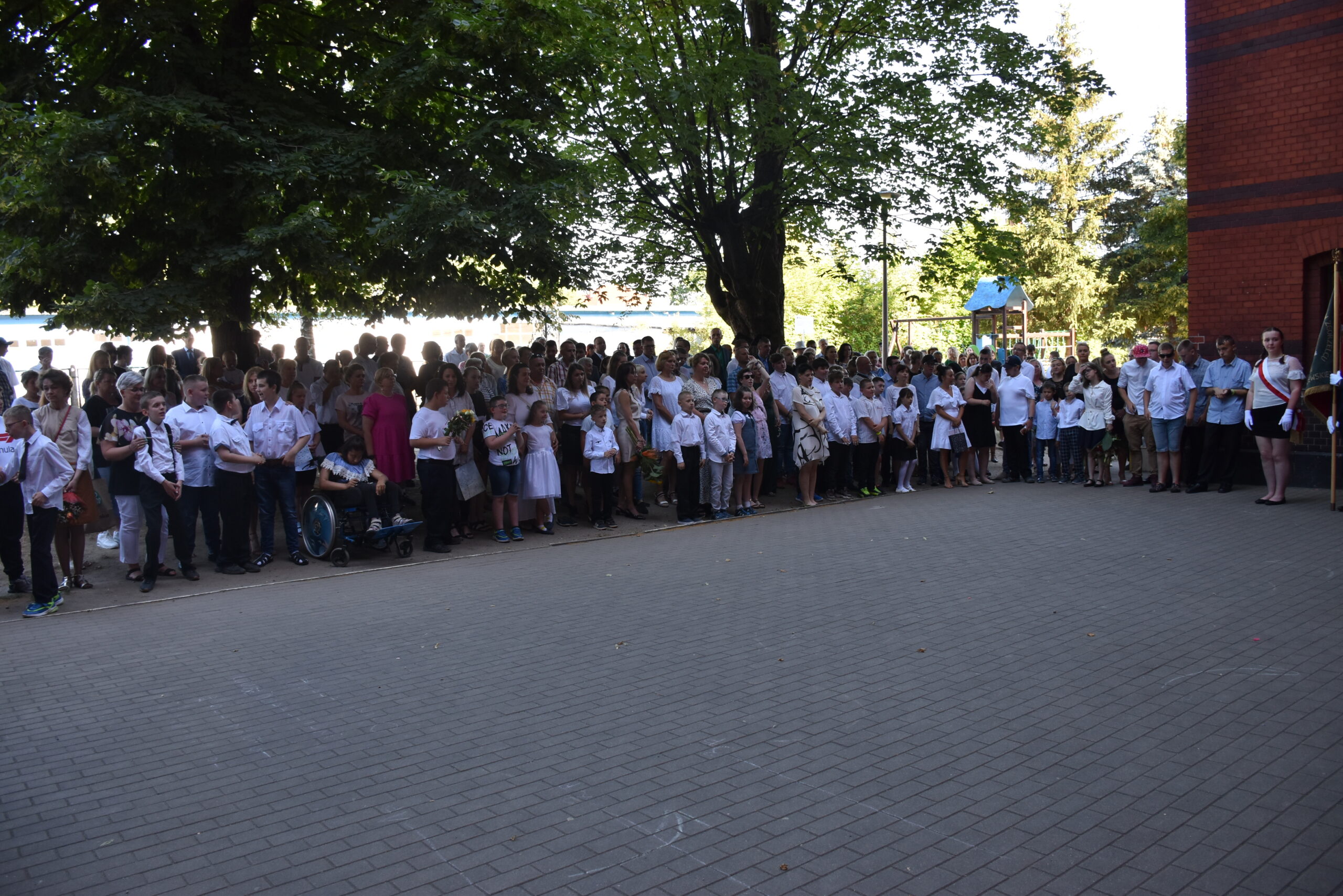 Uczestnicy apelu na koniec roku szkolnego stoją na placu