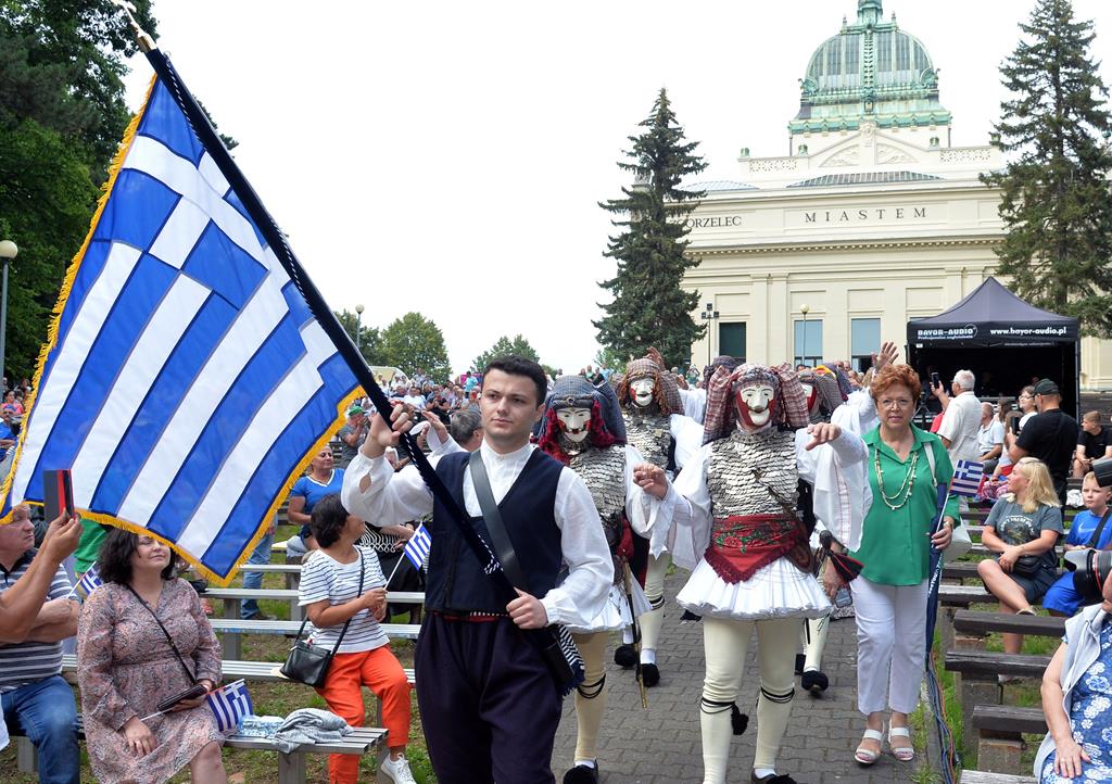 Uroczysty pochód z flagą Grecji, w tle widzowie