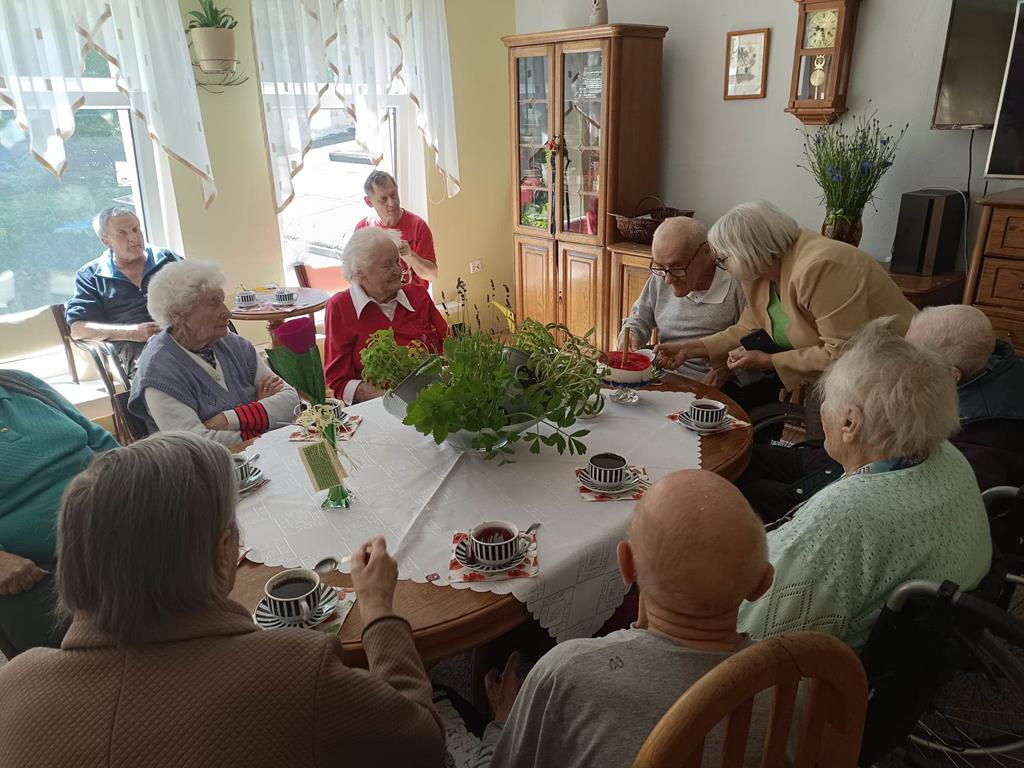 Podopieczni Domu Pomocy Społecznej Ostoja świętują przy stole urodziny mieszkańca.